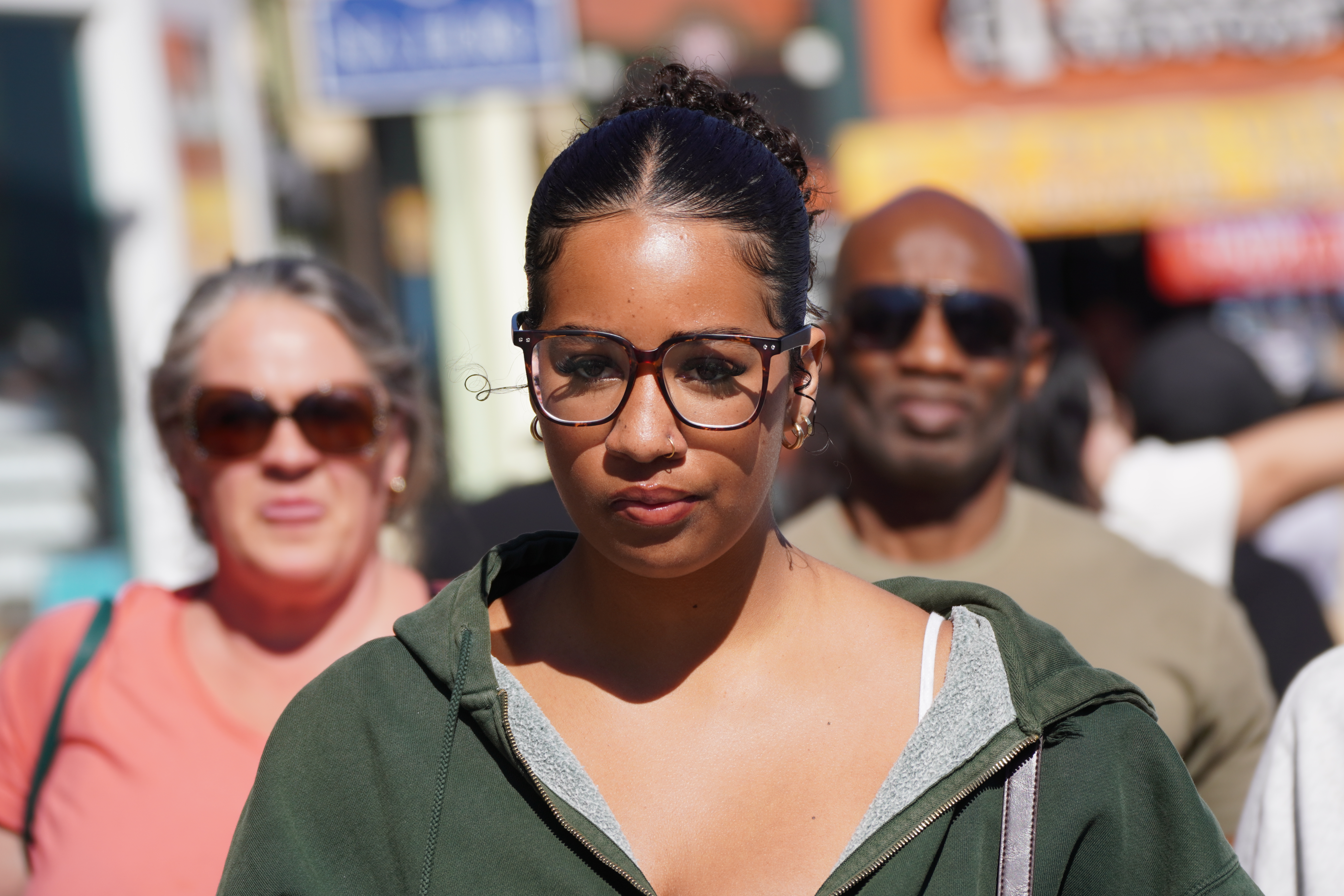Street portrait of a woman with glasses walking toward the camera in bright sunlight