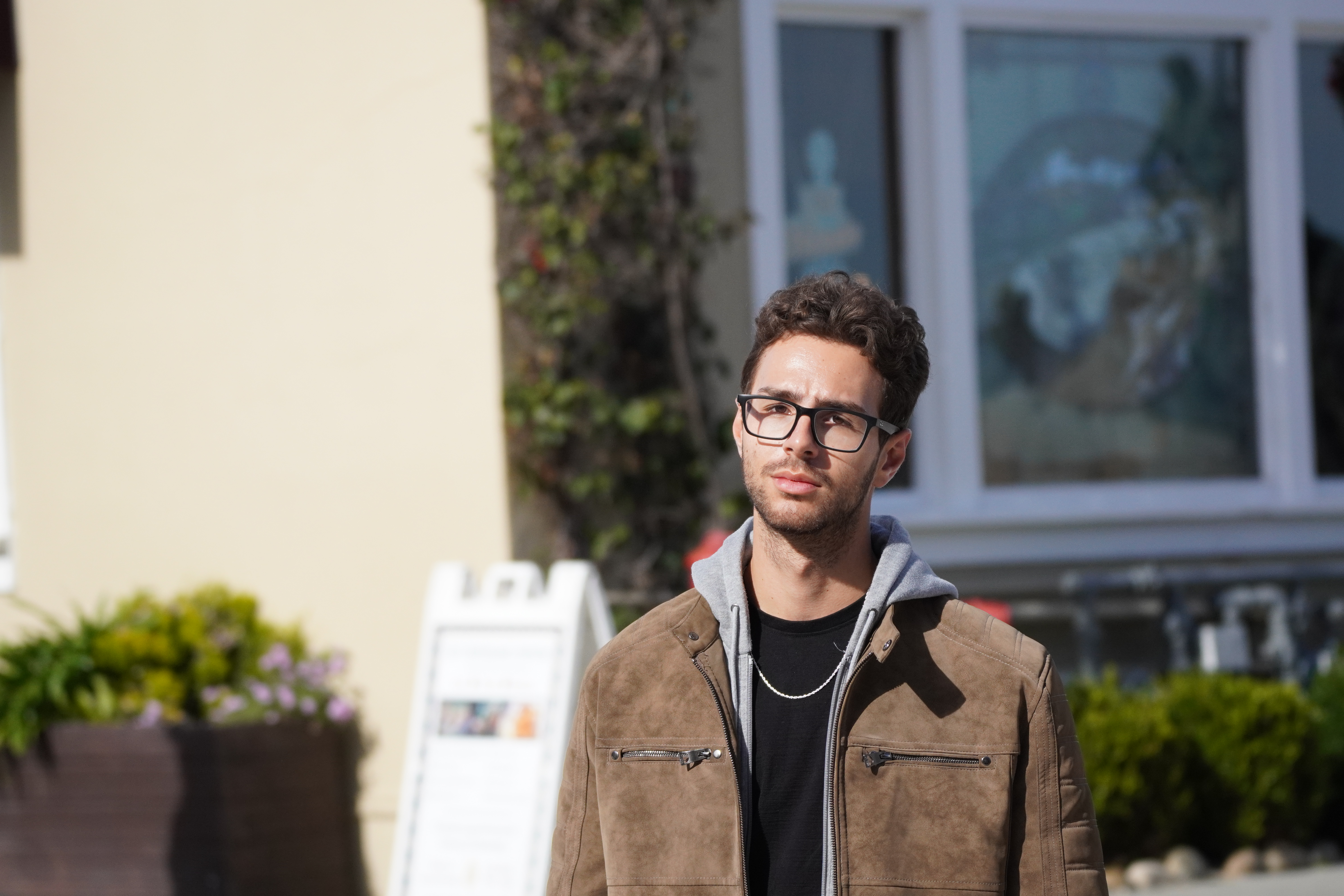 Portrait of a man in glasses and a brown jacket standing outdoors