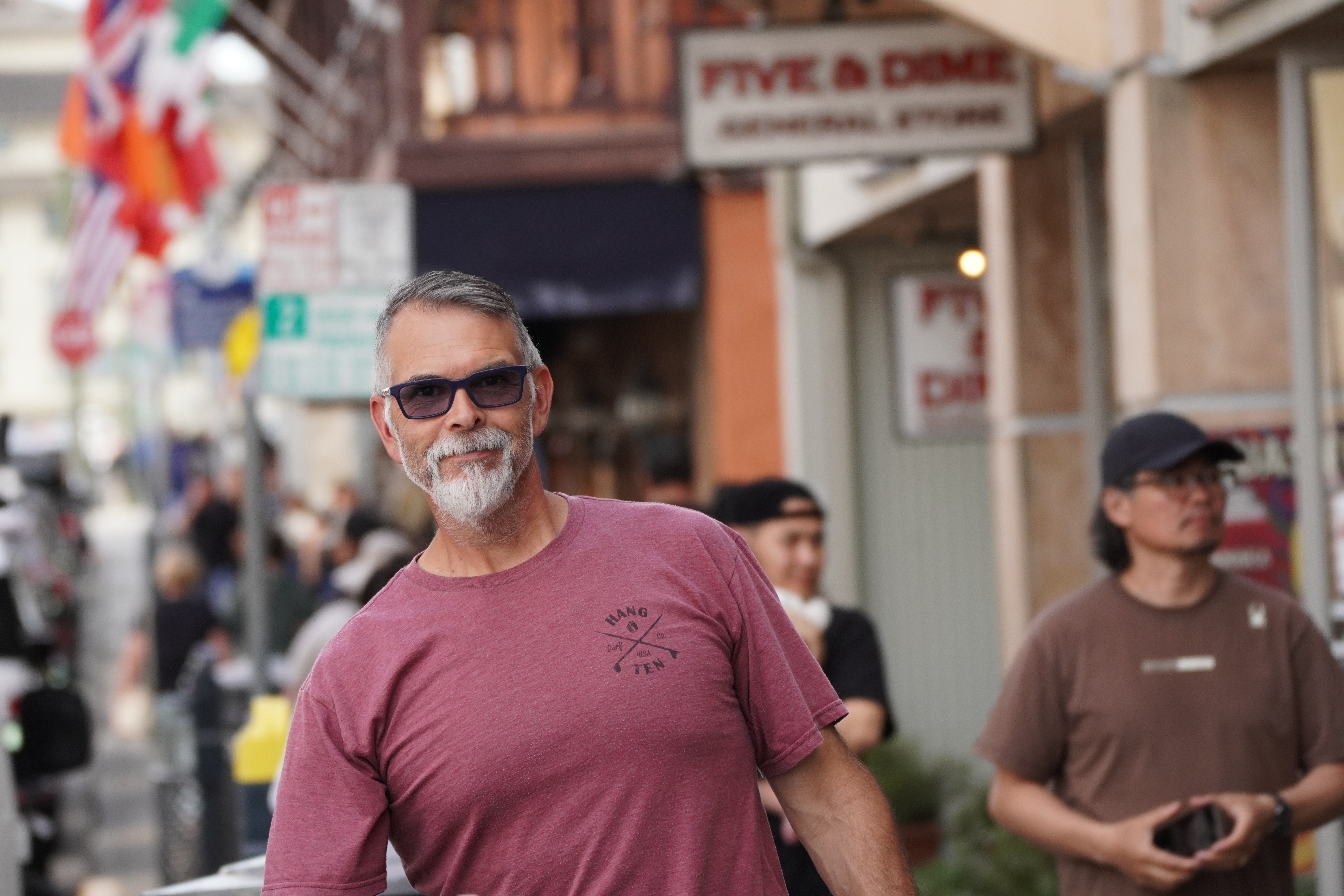 Portrait of a man in a rose-colored shirt standing on a busy street